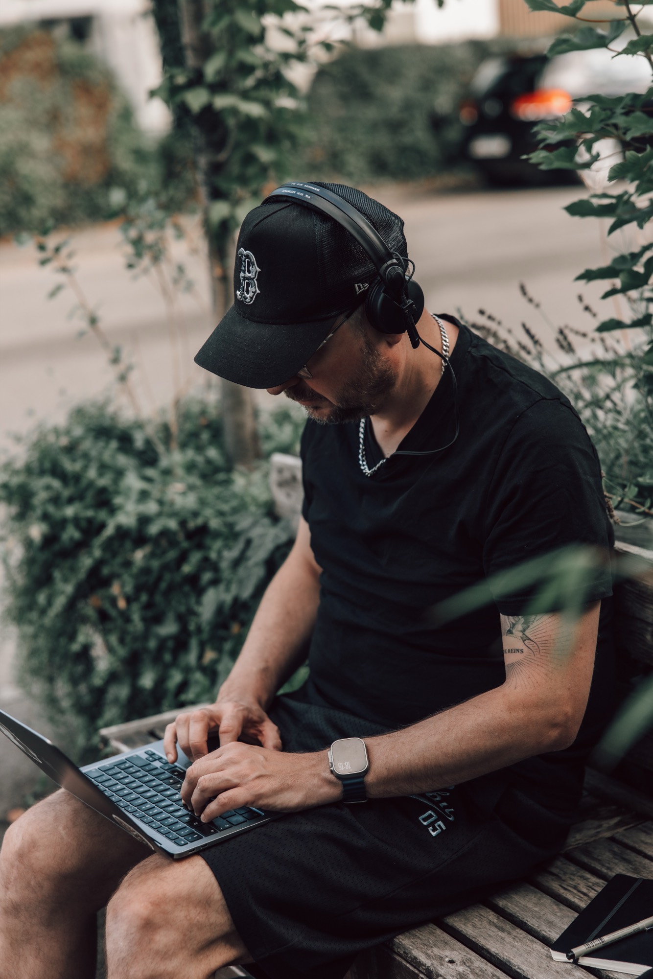 Vaynex working outdoors on a laptop, headphones on